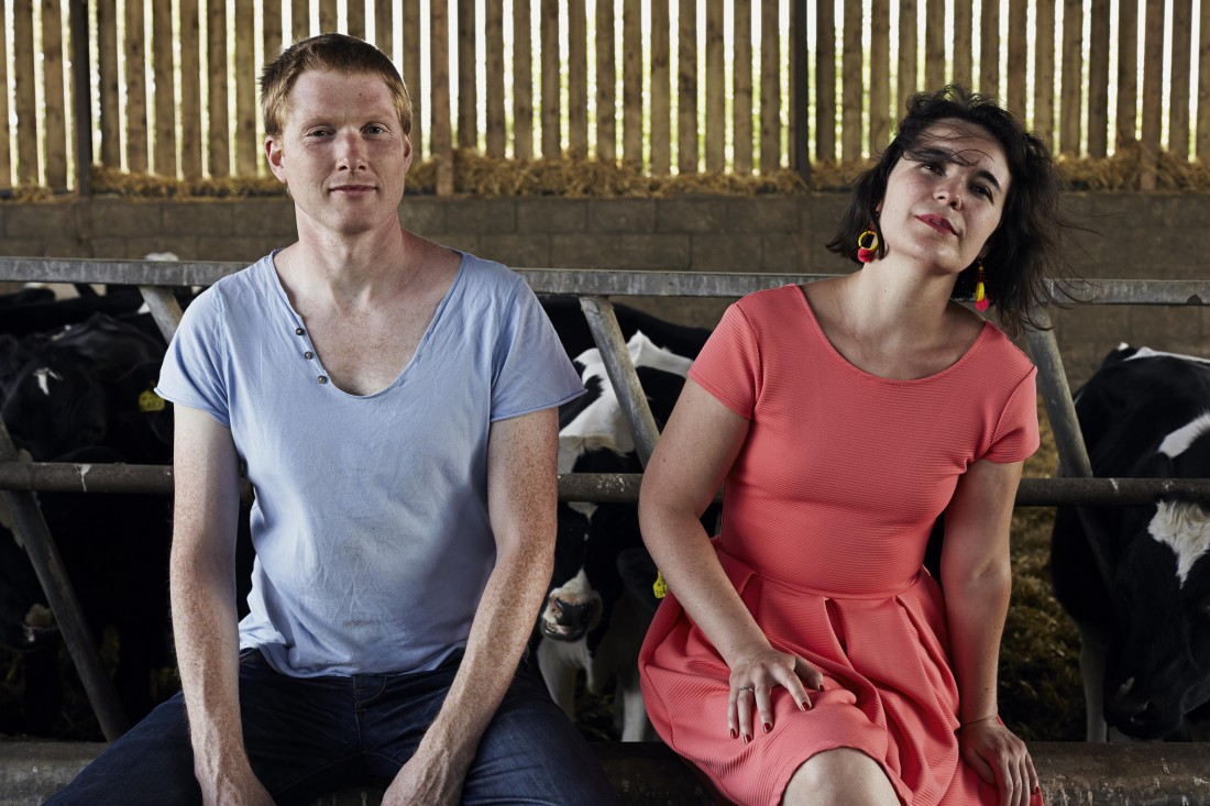 Two Destination Language sat with cows Kat and Alister from Two destination Language are sat in a farm in front of cows